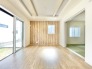 6号棟 お庭へ繋がる大開口窓が、圧倒的な開放感をもたらす心地よい居室。天井の見せ梁や木目調のアクセントクロスが、空間に洗練された印象を与えます。引き戸を開ければ和室と一体になり、ライフスタイルに合わせてフレキシブルに使えるのが魅力。家族みんながホッと安らぐ、居心地の良い特等席です。