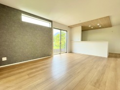 シックなアクセントクロスが空間を引き締め、木目の温もりと調和する落ち着いた住まい。すっきりとした設計が開放感を生み出し、外の緑とつながるゆとりある暮らしを予感させる洗練された空間です